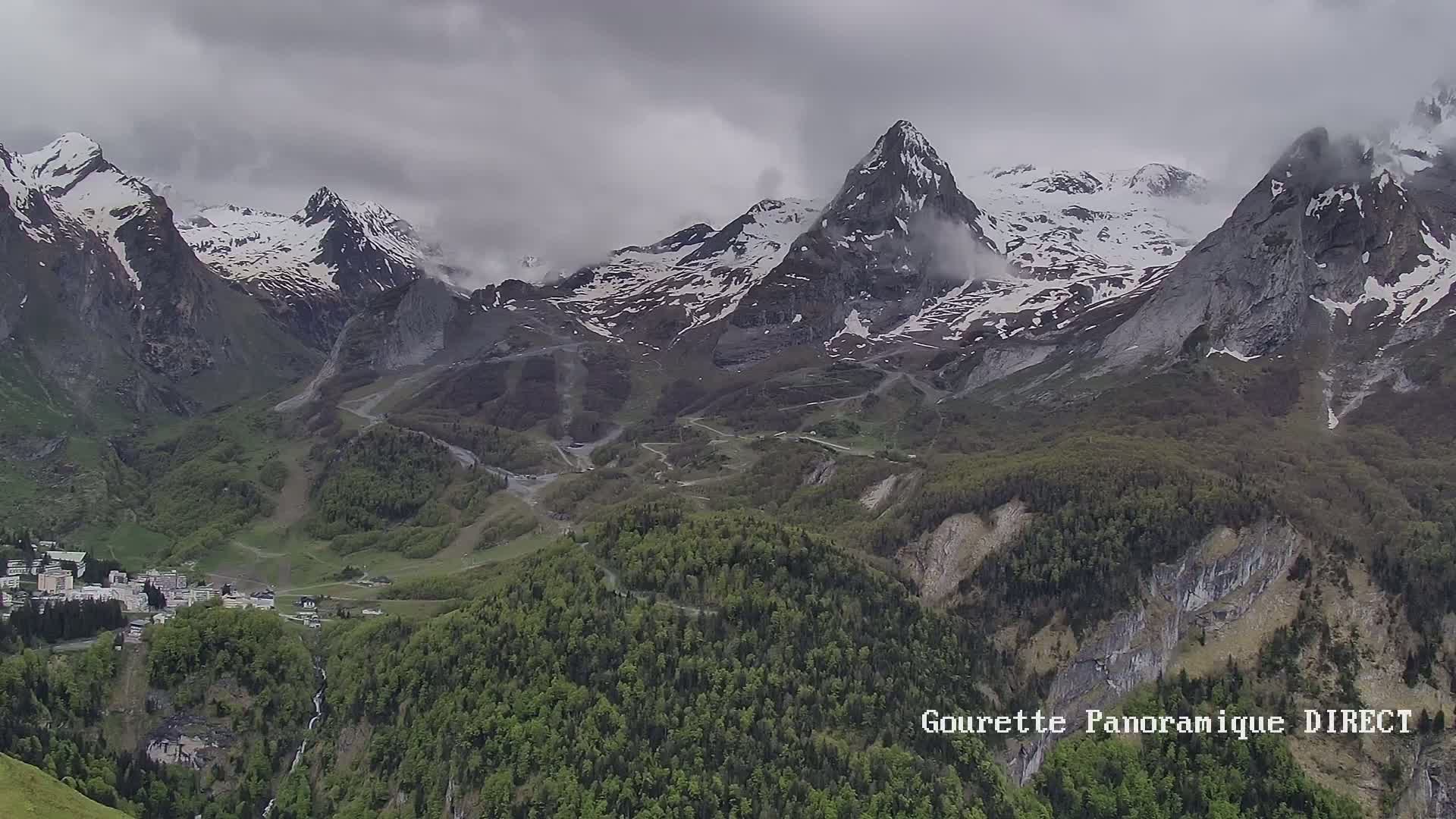 A mountain village nestled in a valley below snow-capped peaks under an overcast sky.