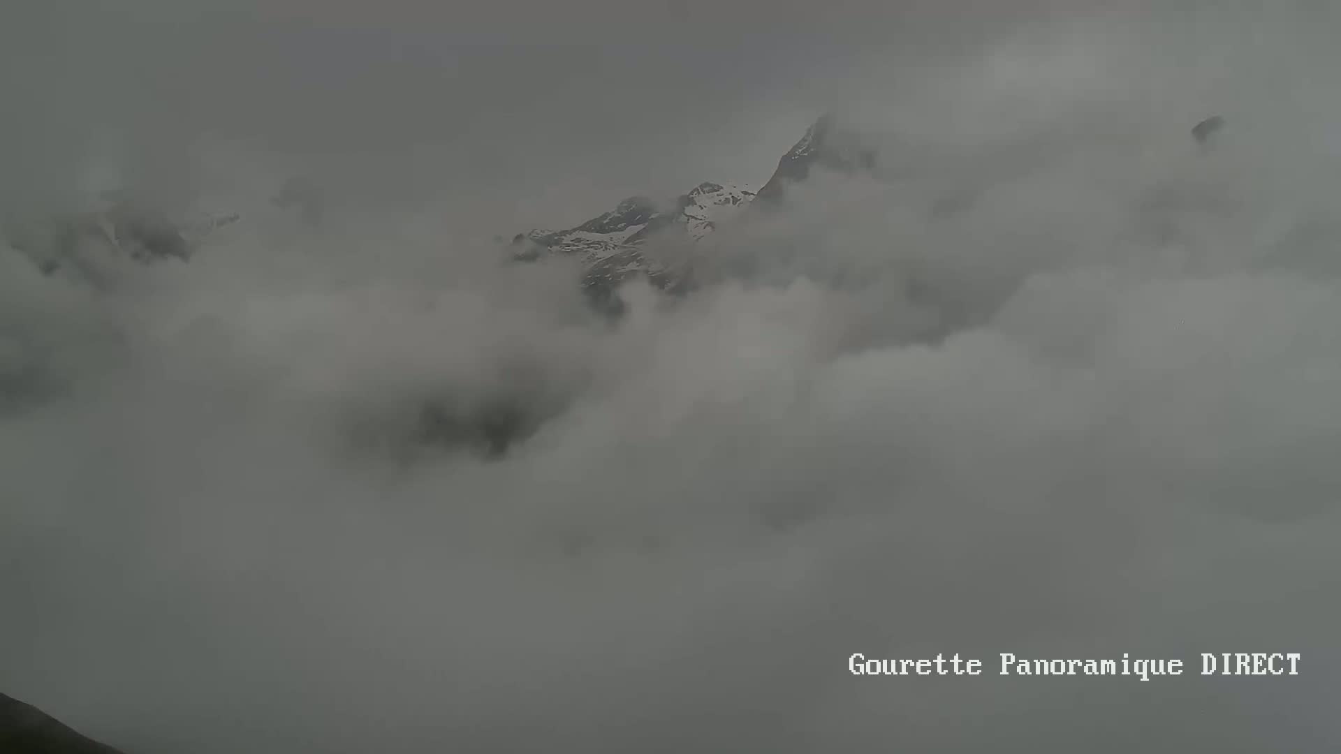 A snow-capped mountain peak is partially obscured by a thick, gray fog.