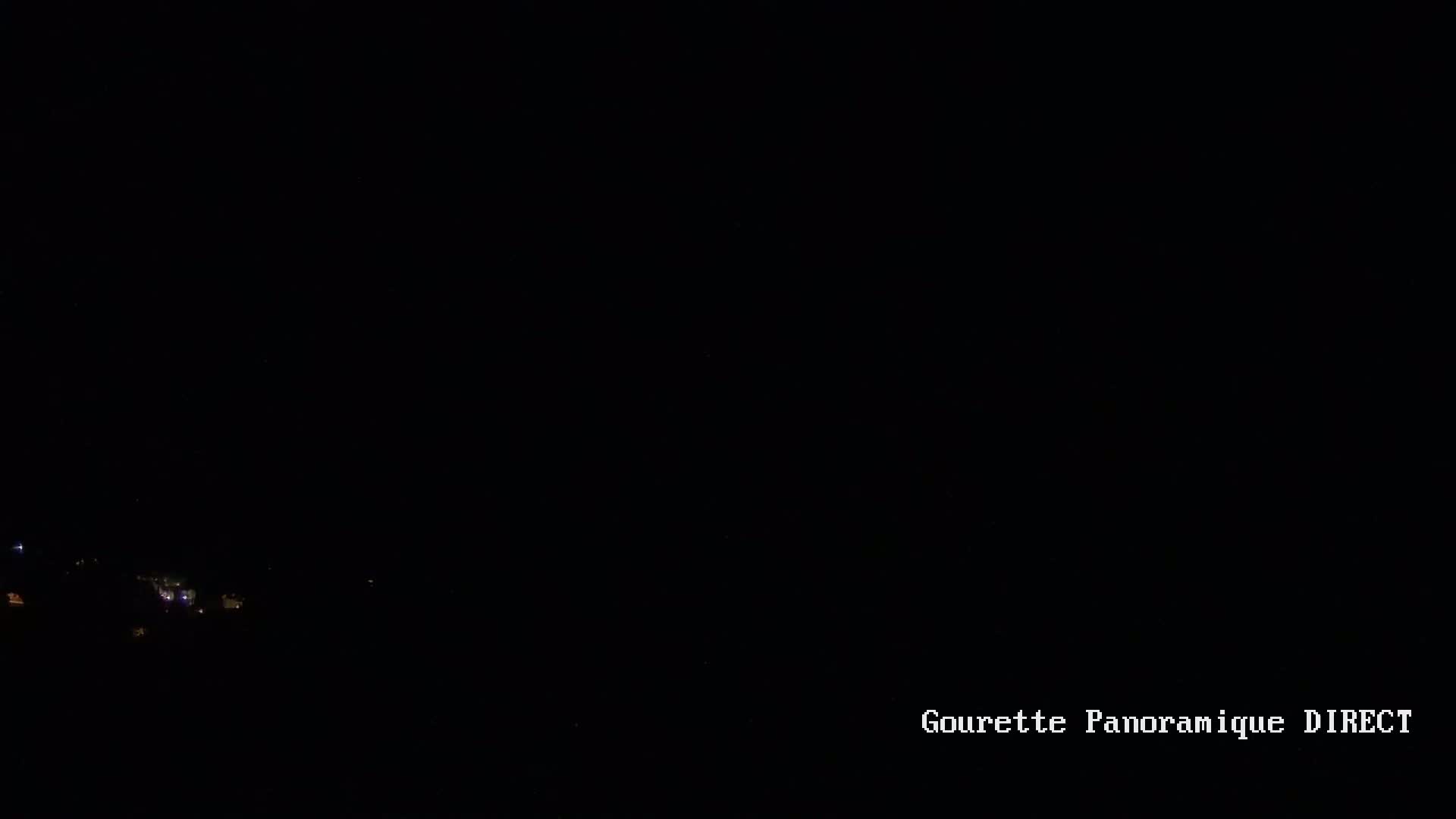 A dark, nighttime scene shows a few faint lights in the distance.
