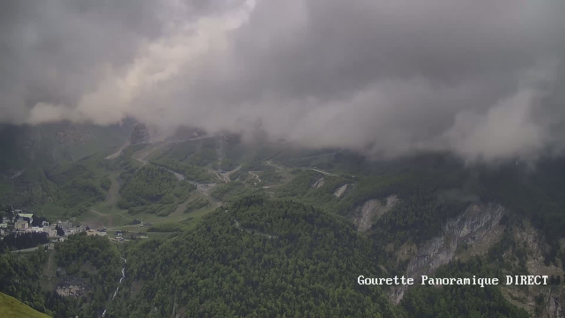 A mountainous landscape is partially obscured by low-hanging clouds, with a small town visible in the valley below.