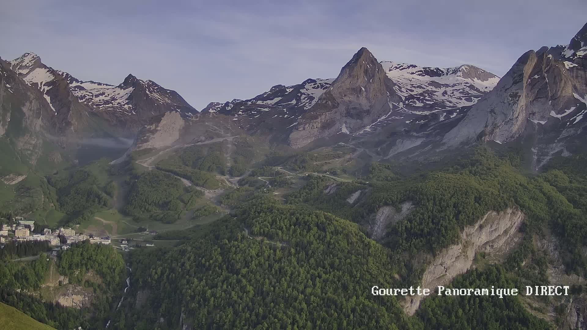 A mountain village nestled in a valley below snow-capped peaks on a clear day.