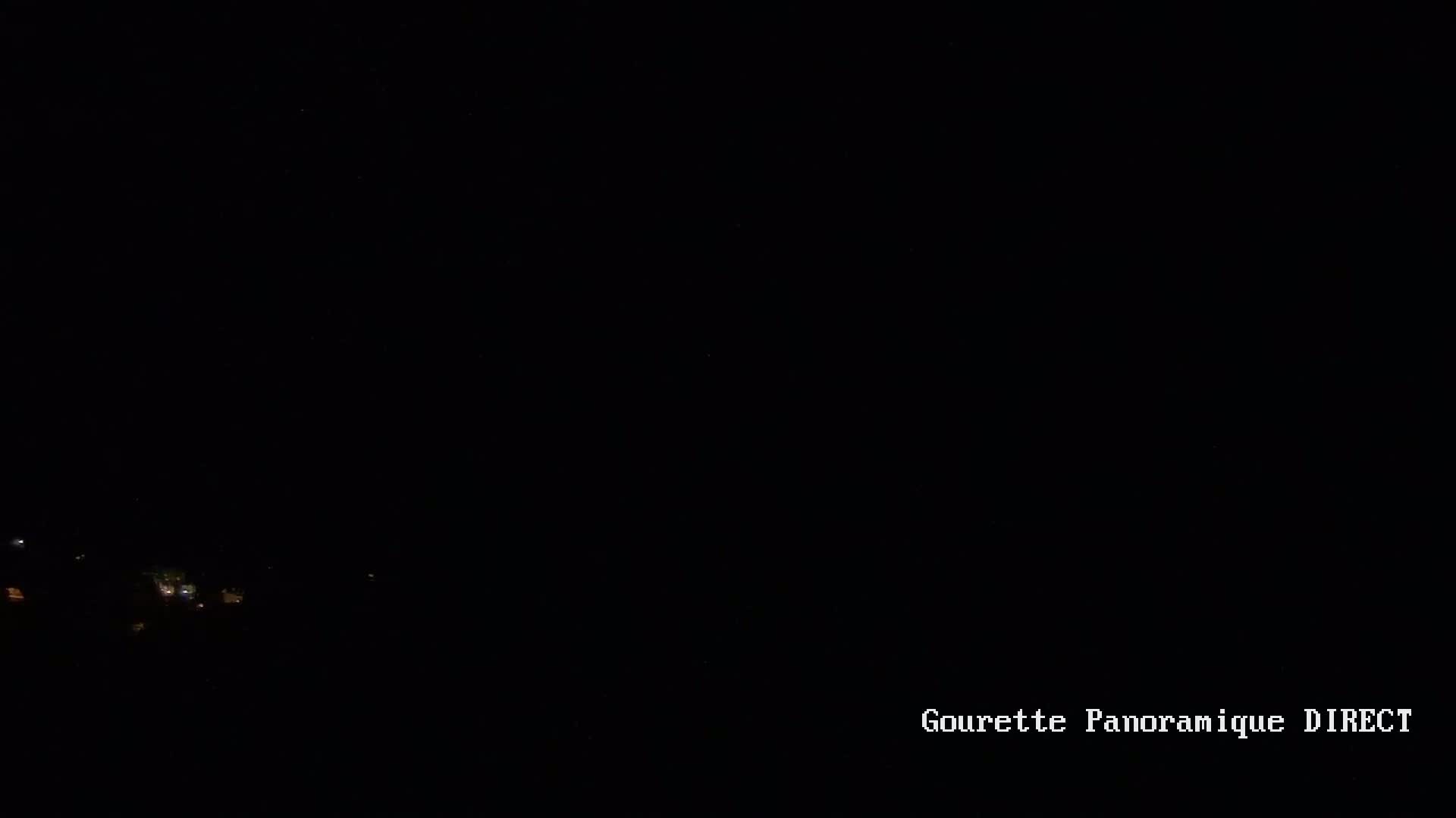 A nighttime view of dimly lit buildings in the distance under a dark, clear sky.