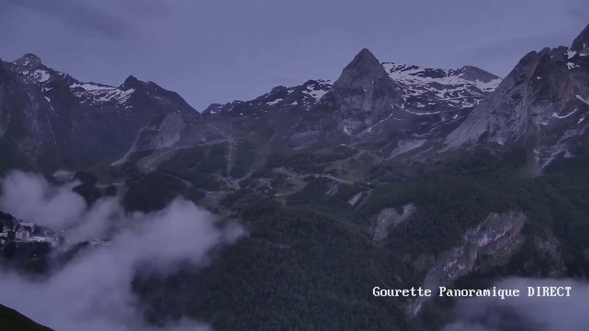 Snow-capped mountains rise above a valley shrouded in low-lying clouds at dusk.
