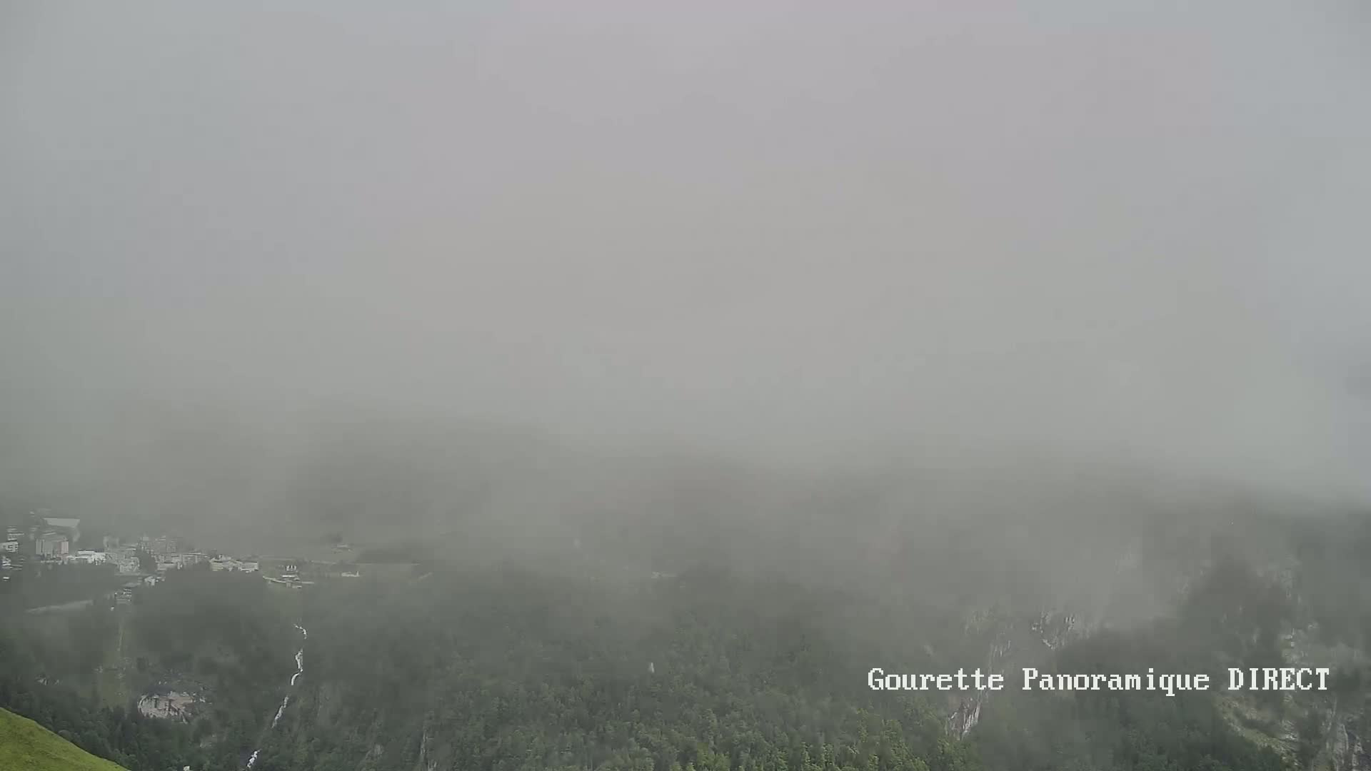 A foggy view shows a valley with a small town and forested hillsides in the distance.