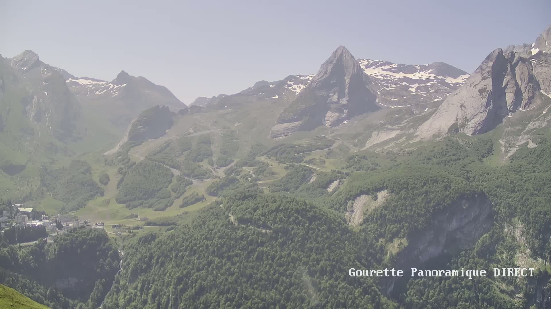 A hazy, long-range view shows a valley nestled between steep, snow-dusted mountains, with a small town visible in the lower left.