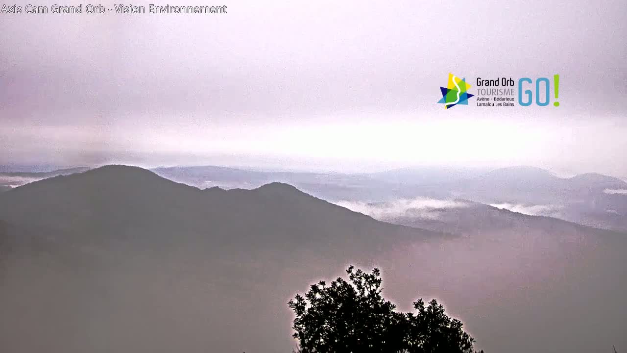 A hazy, mountainous landscape is visible, with low-lying fog or clouds in the valleys.