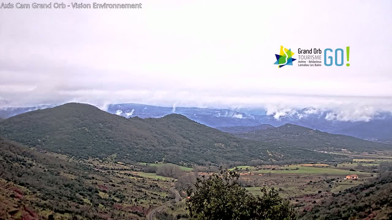 A misty, overcast landscape of rolling green hills and valleys stretches to distant mountains under a cloudy sky.