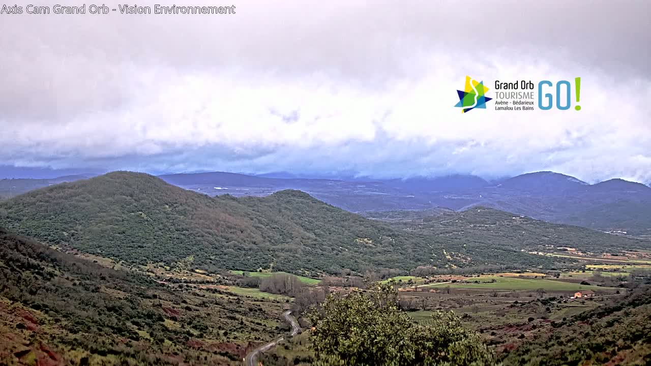 A winding road leads through a hilly landscape under a cloudy sky.