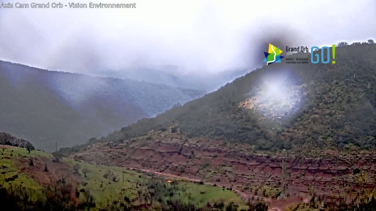 A misty view of rolling hills and valleys, showing exposed reddish-brown earth and sparse vegetation.