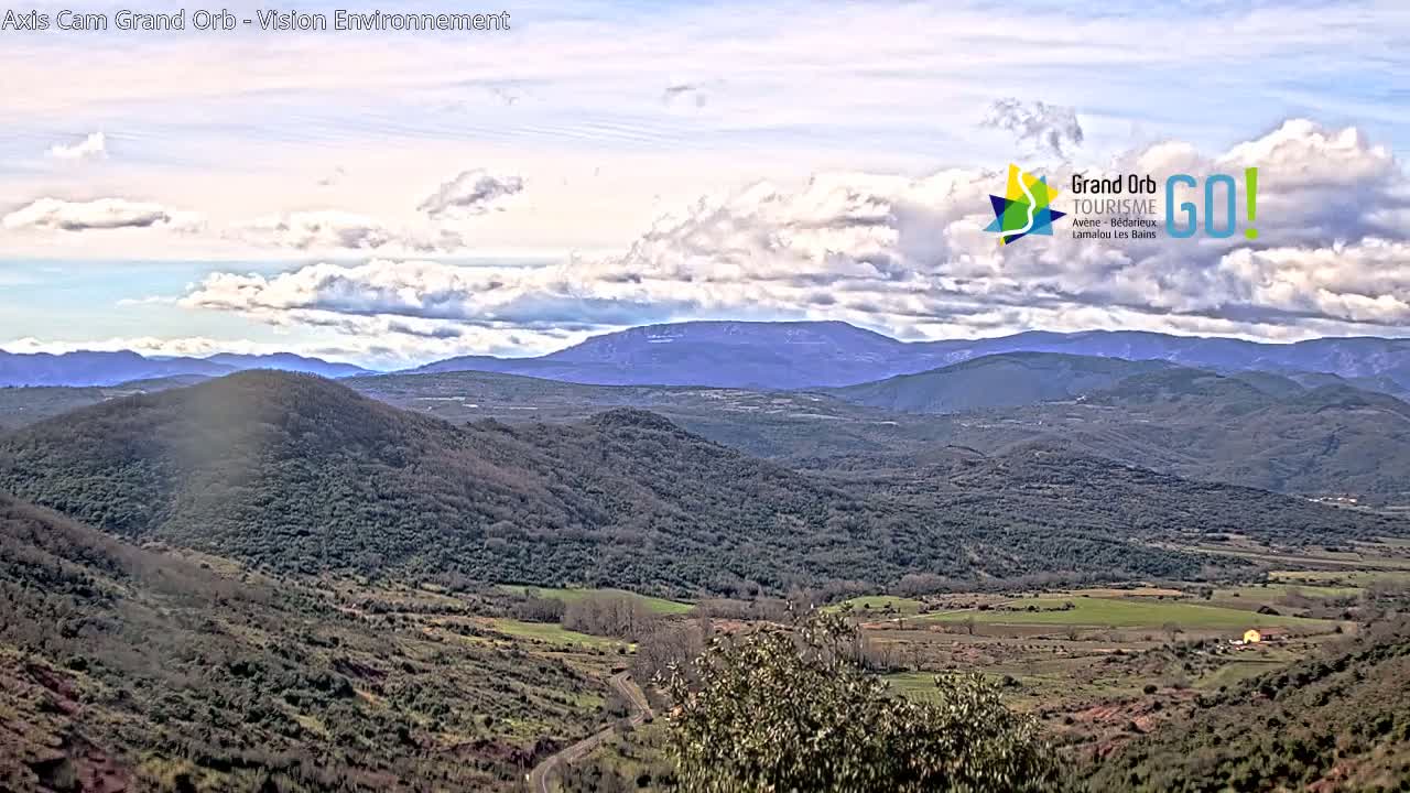 A partly cloudy day reveals a sprawling landscape of rolling hills and valleys, extending to distant mountains under a bright sky.