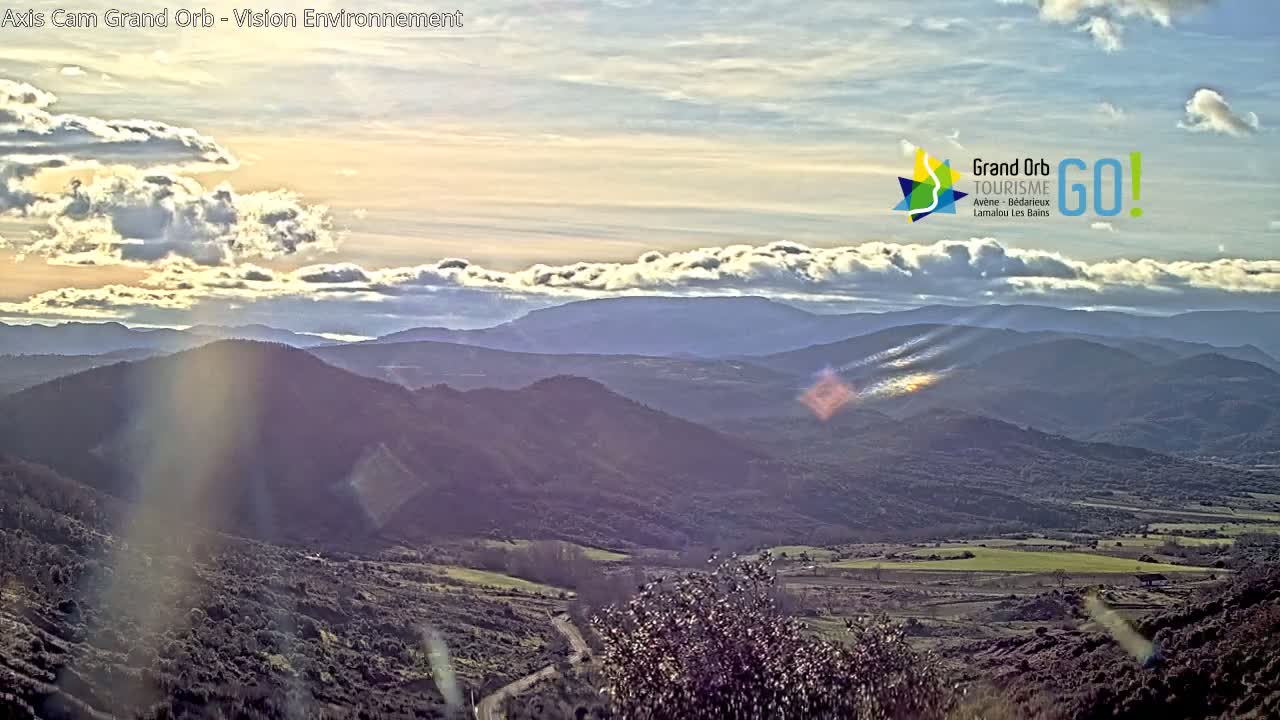 A sunlit view of rolling hills and valleys under a partly cloudy sky.