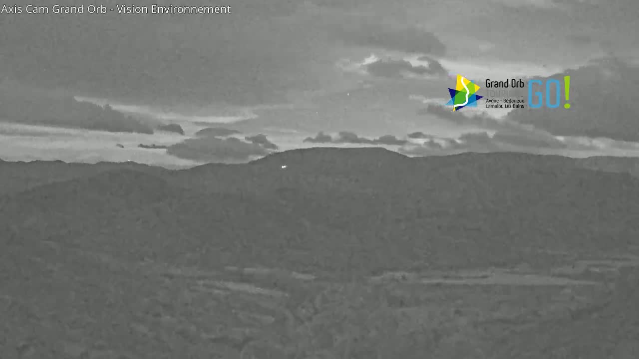A mostly cloudy, dusky sky overlooks a dark, hilly landscape.