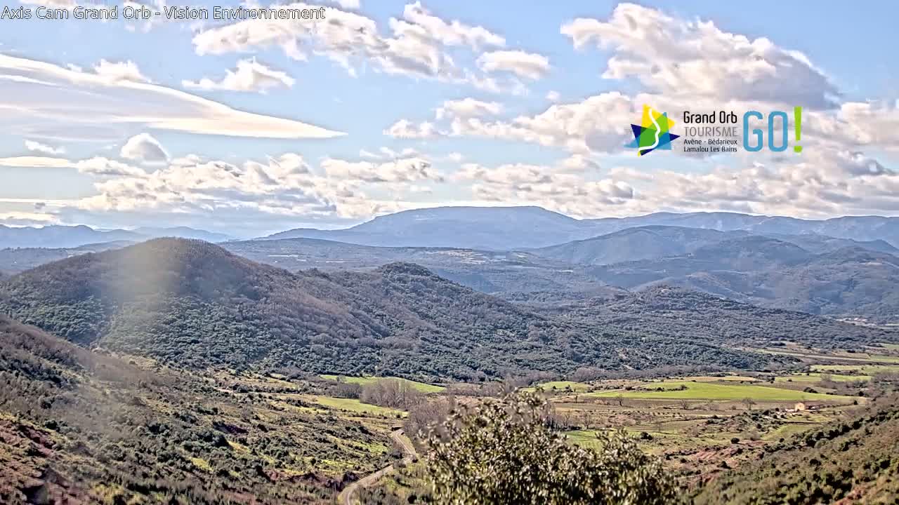 A panoramic view of rolling hills and distant mountains under a partly cloudy sky.