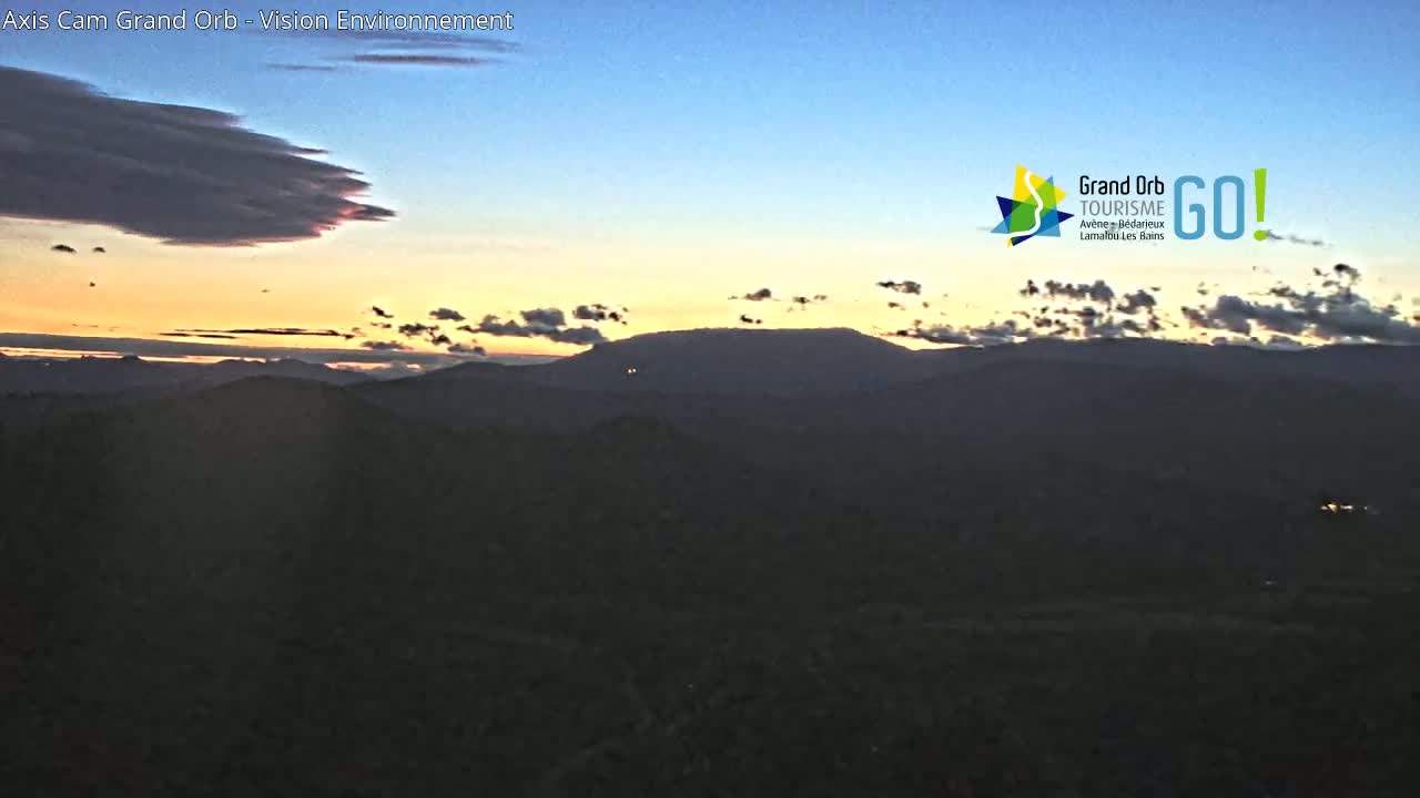 A sunset over a mountainous landscape with a mostly clear sky, featuring some clouds near the horizon.
