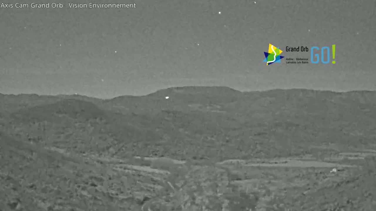 A nighttime, grayscale image shows a hilly landscape under a clear, dark sky.