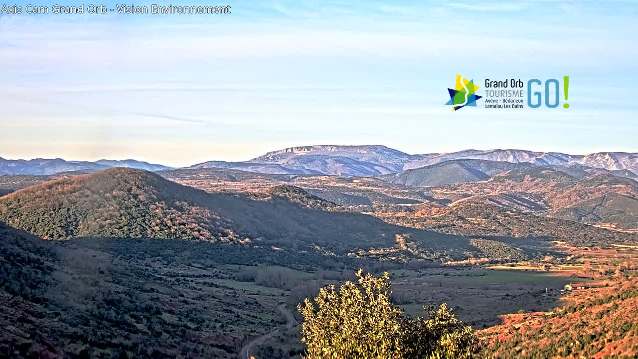 A panoramic view of a hilly landscape under a clear sky, showing rolling hills and distant mountains.