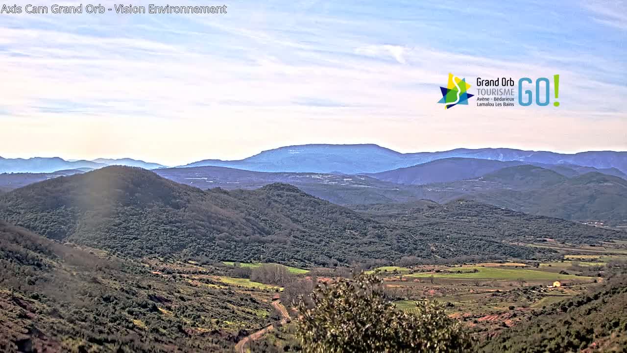 A vast, mountainous landscape under a mostly clear sky displays rolling hills and valleys covered in low-lying vegetation.