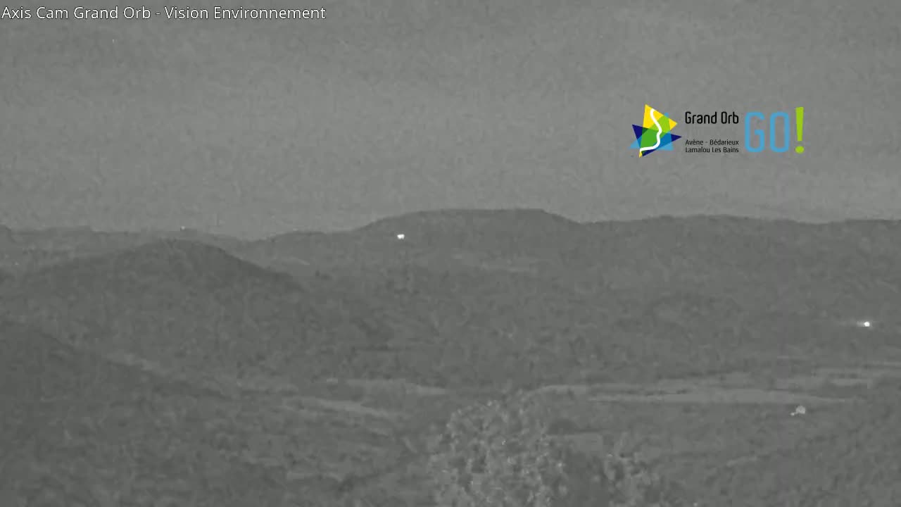 A nighttime grayscale image shows a hilly landscape under a dusky sky.