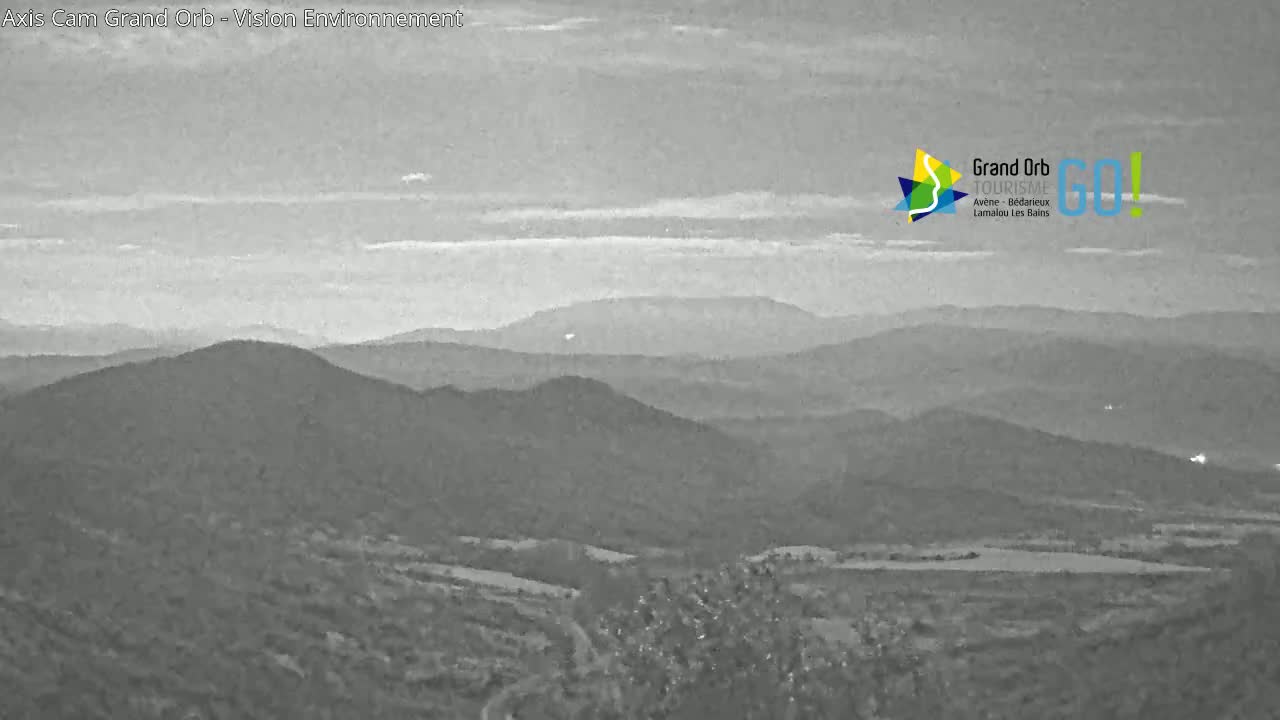 A grayscale long shot shows a mountain range under a hazy sky.