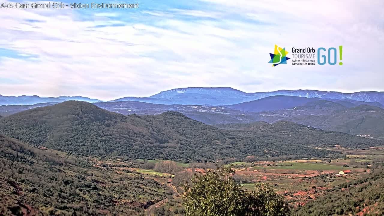 A panoramic view of rolling hills and distant mountains under a mostly cloudy sky.