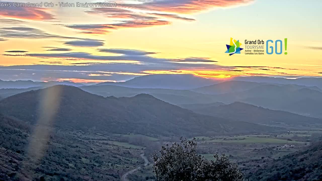 A sun setting over rolling hills and valleys under a partly cloudy sky.