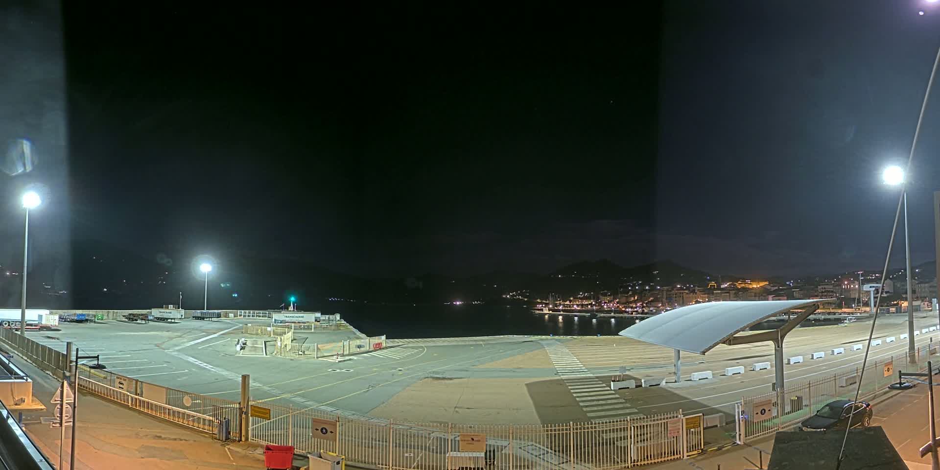 An empty, brightly lit port area at night, with a city skyline visible in the distance under a clear, dark sky.