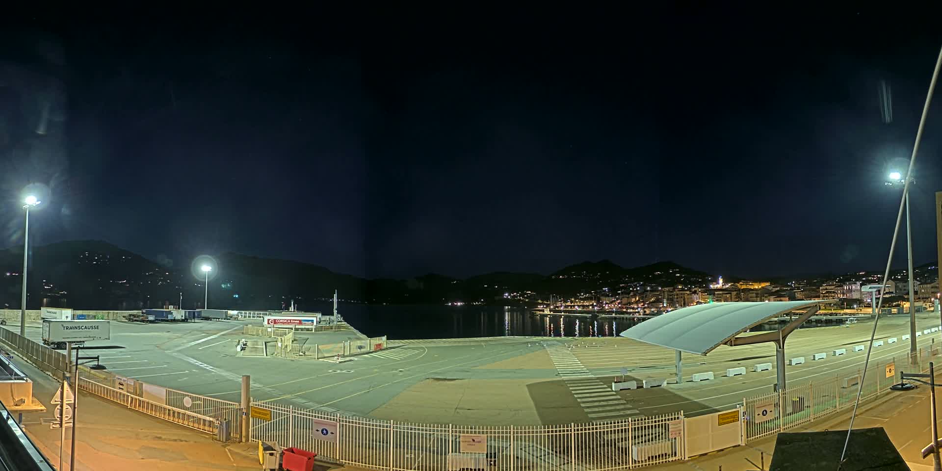 A nighttime view of a brightly lit port area with several trucks and a city skyline in the background.