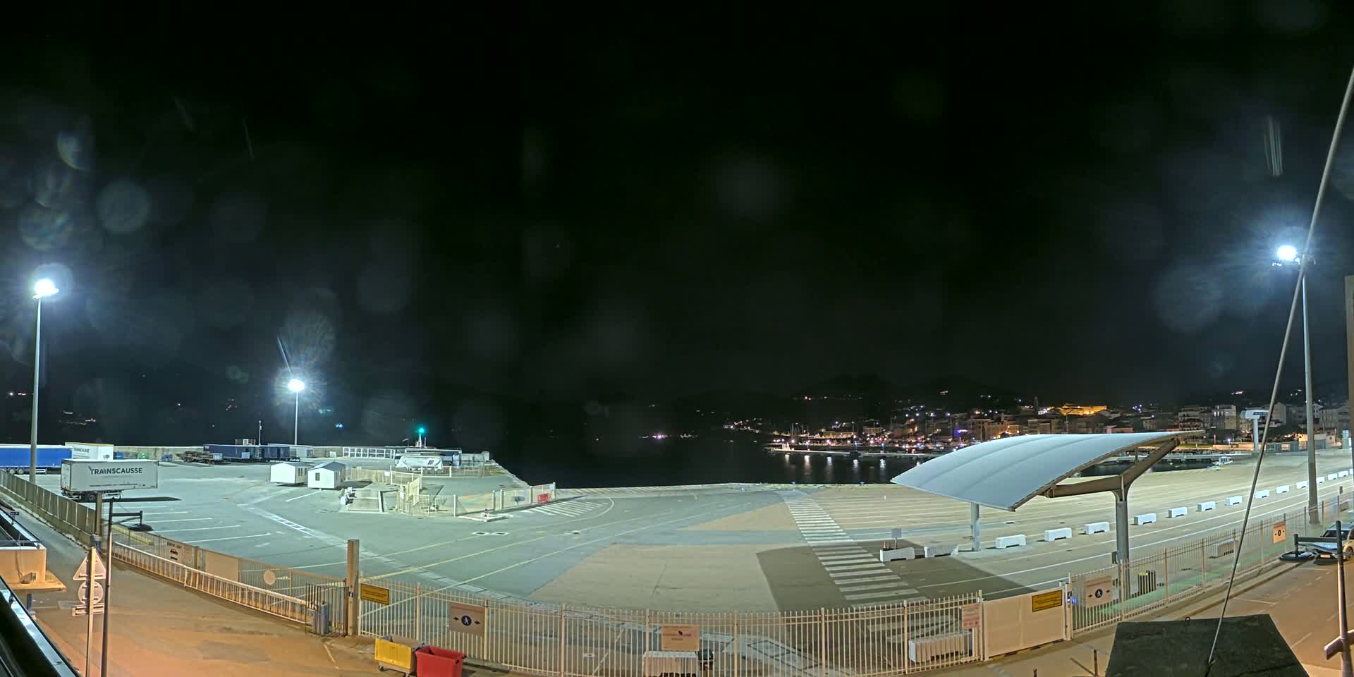 An empty, nighttime port area with a few parked trucks and cars, under a dark, slightly hazy sky.