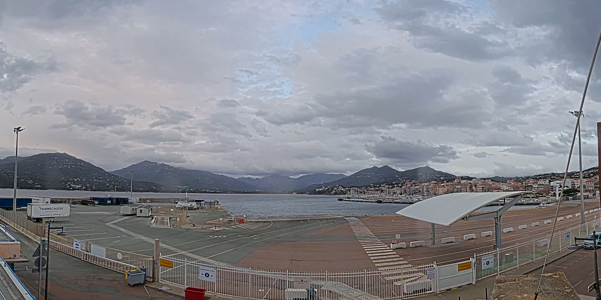 A mostly empty port area with a harbor and distant mountains under a cloudy sky.