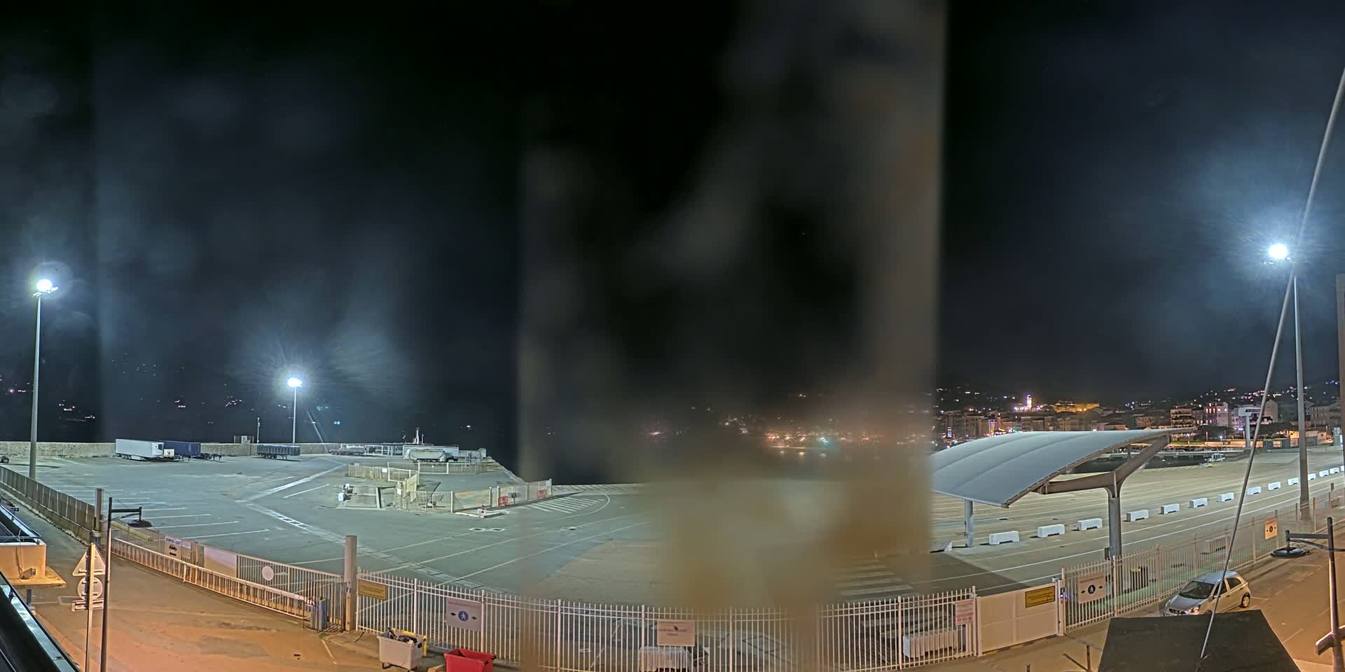 A nighttime view of an empty, well-lit port area with a few parked vehicles, under hazy conditions.