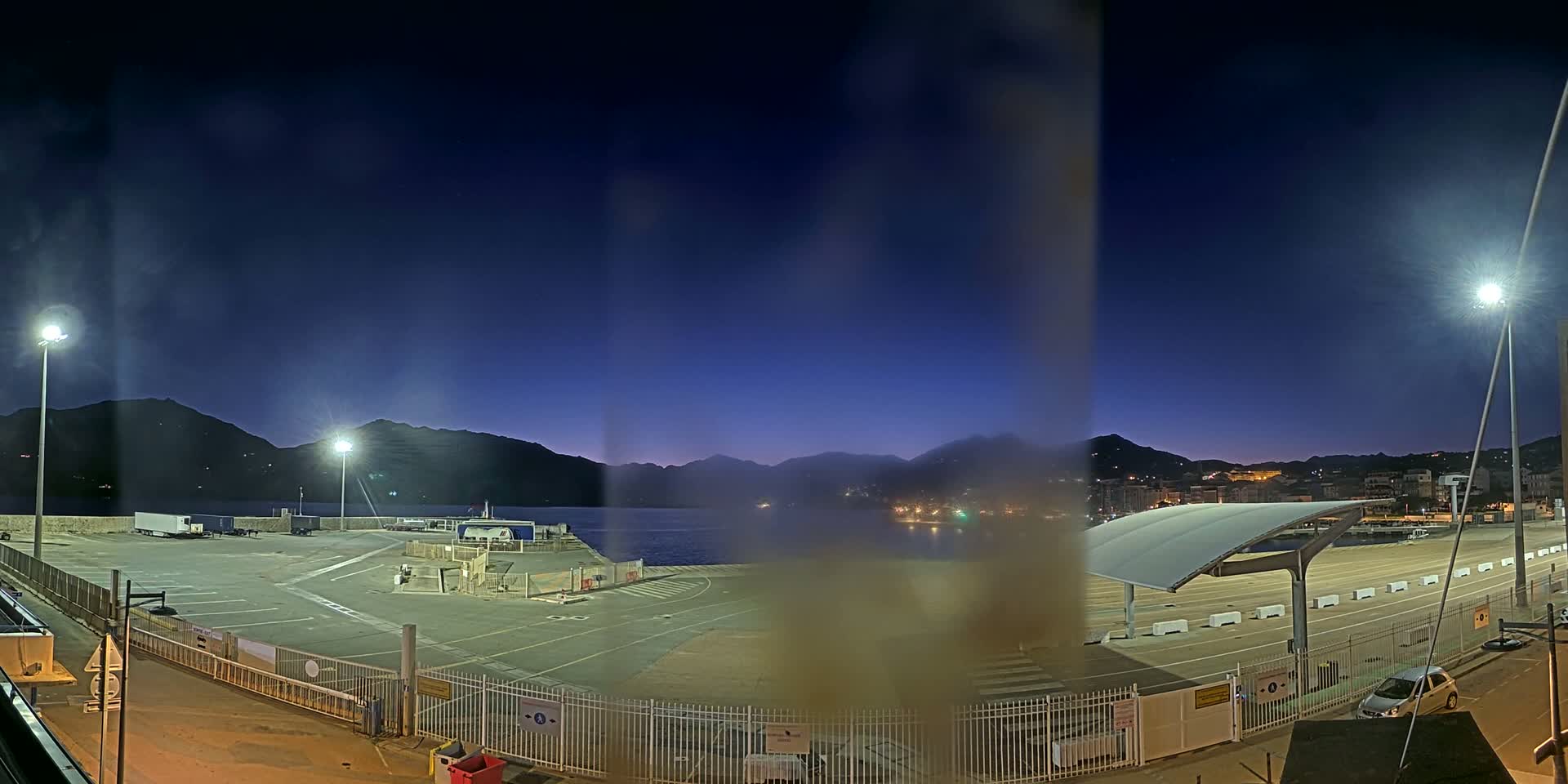 A nighttime view of an empty port area with mountains in the background under a dark blue sky.