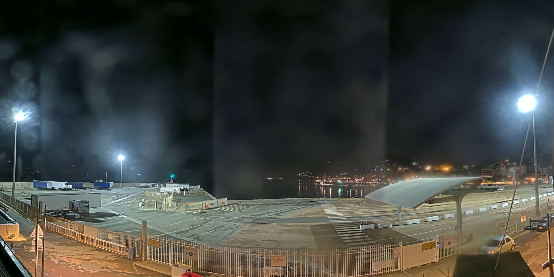 A nighttime view of an empty port area with several trucks parked, under a dark, hazy sky.