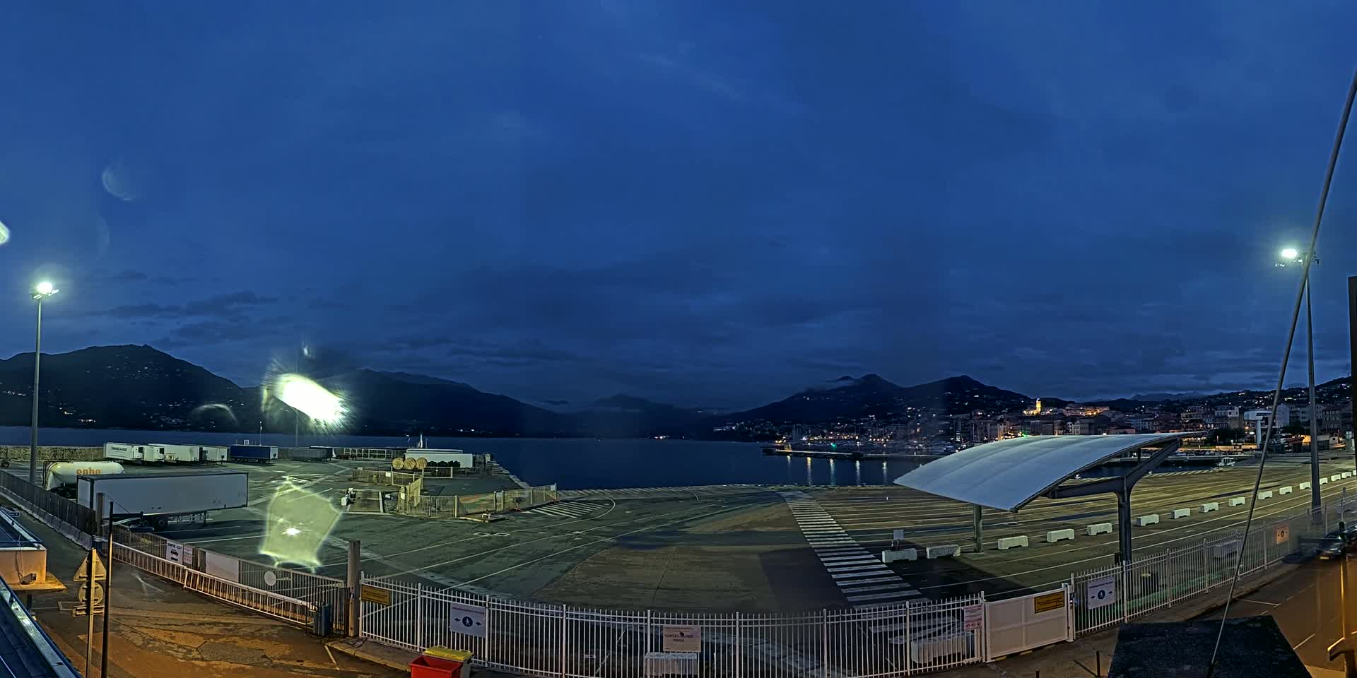 An empty, dark port area at twilight, overlooked by mountains under a mostly clear, blue-ish night sky.
