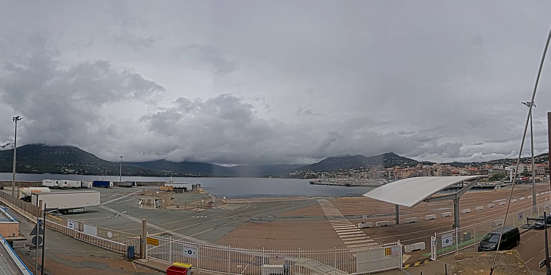 A port with several semi-trailer trucks, a small town in the distance, and overcast skies.