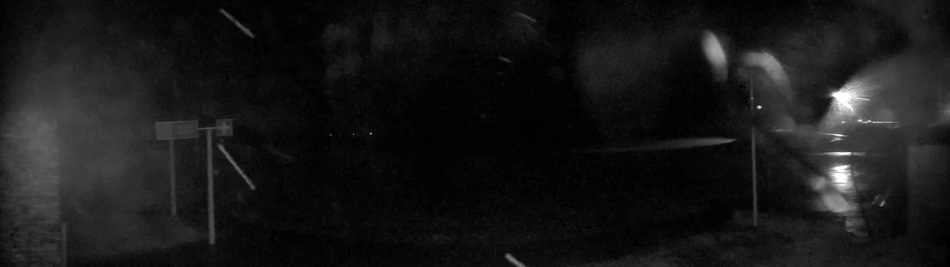 A dark, snowy night scene shows a road with indistinct objects and blurry lights in the distance.