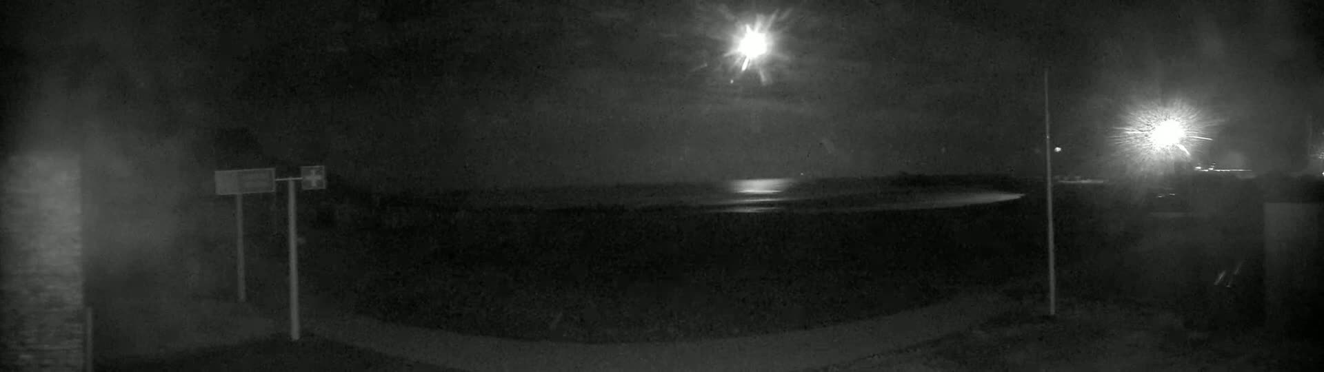 A nighttime view of a calm body of water under a bright moon, with a few lights visible in the distance.