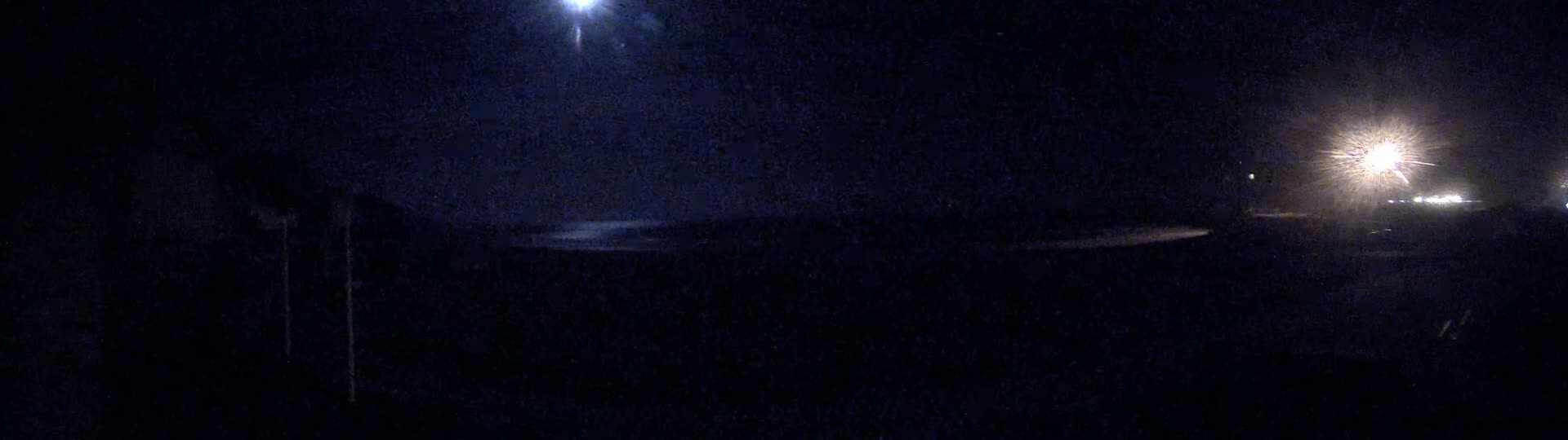 A dark nighttime scene shows a body of water under a bright moon and distant lights.