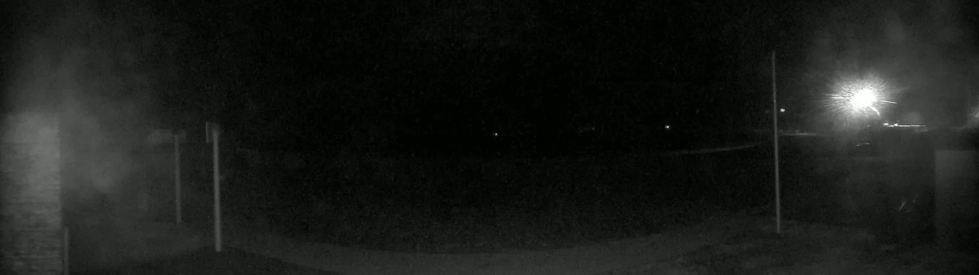 A nighttime, low-light view of a dark, paved area illuminated by a bright light source in the distance.