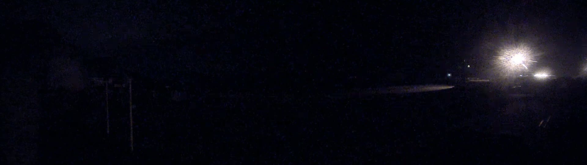 A dark, nighttime scene shows bright headlights in the distance on a road.