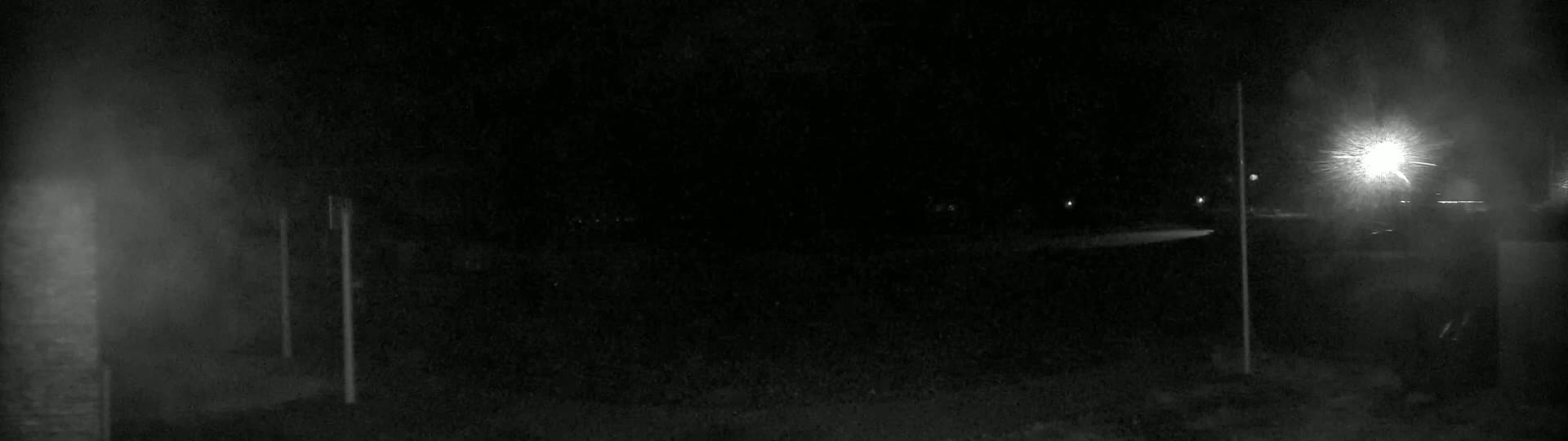 A dark, nighttime scene shows a mostly empty area with two vertical poles and a bright light in the distance.