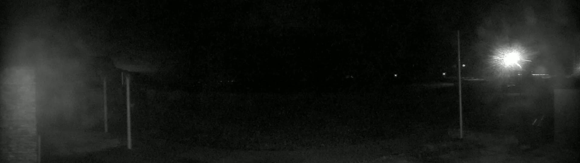A nighttime, low-light image shows a dark, empty area with indistinct objects and a bright light source in the upper right corner.