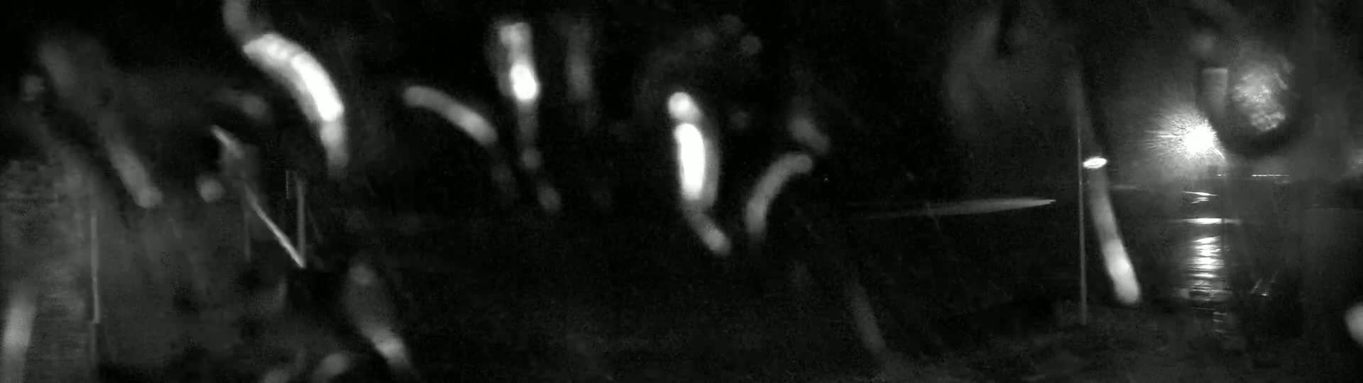 Rain streaks across a blurry nighttime scene showing indistinct shapes and lights.