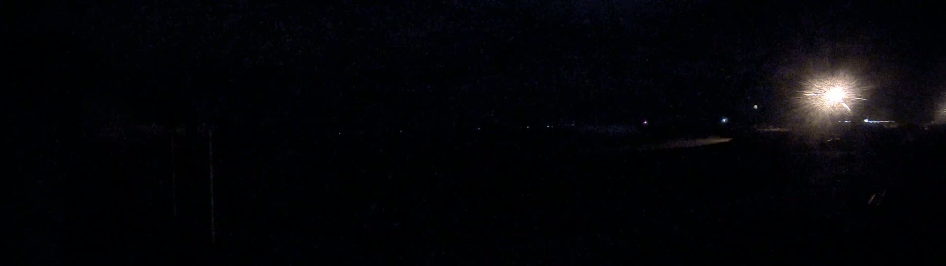 A dark, nighttime scene shows several distant lights and a bright light source in the upper right corner.