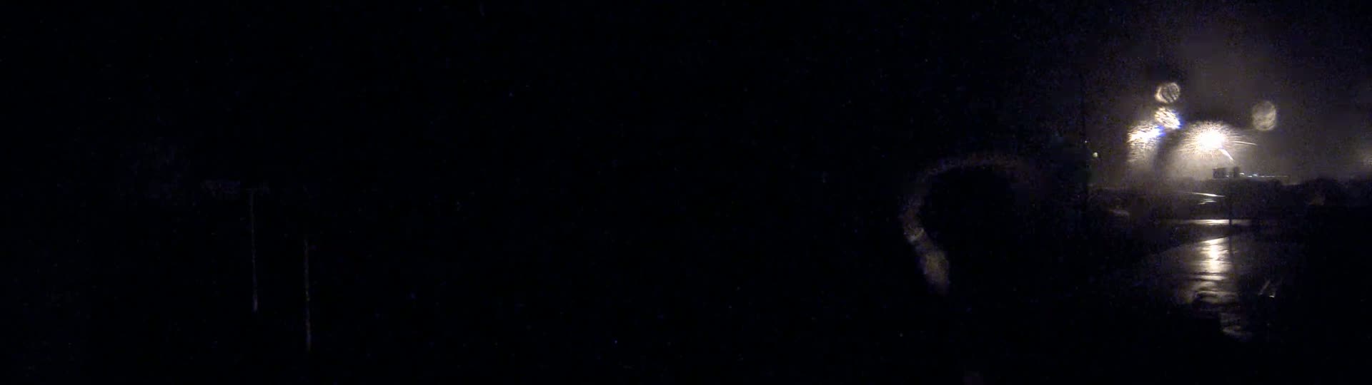 Fireworks explode in the night sky over a rain-slicked road.