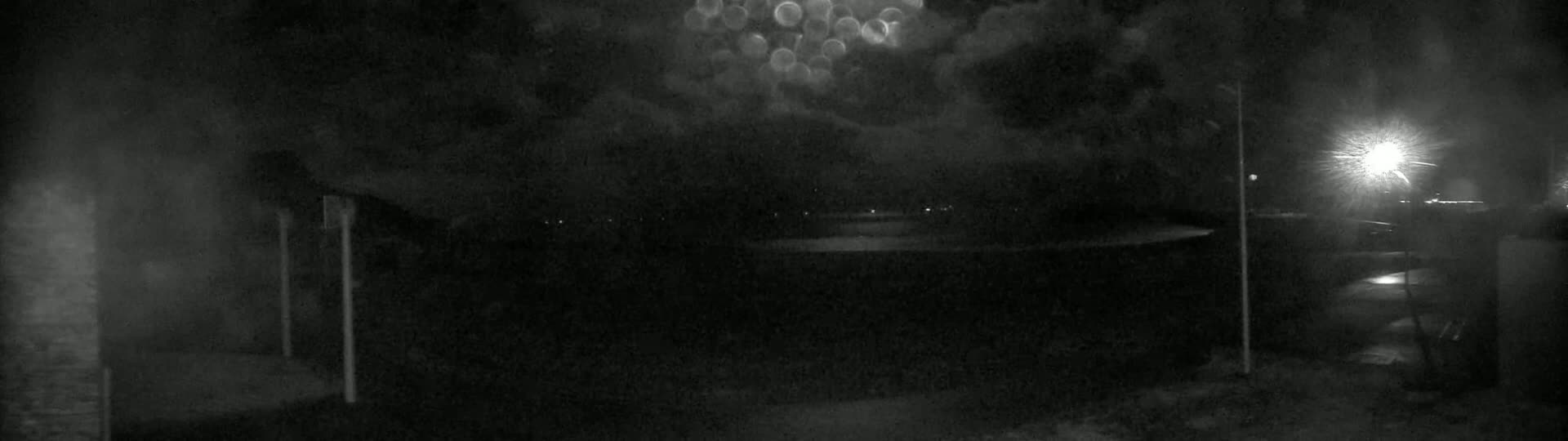A nighttime outdoor scene shows a dark, overcast sky with a few distant lights visible in the darkness.