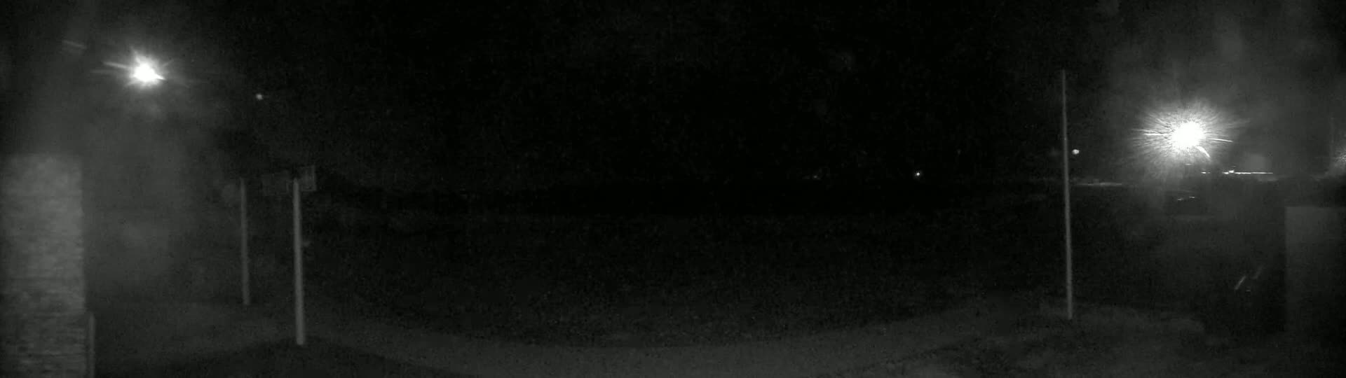 A nighttime outdoor scene shows a dark, empty area illuminated by two bright lights, one on each side of the frame.