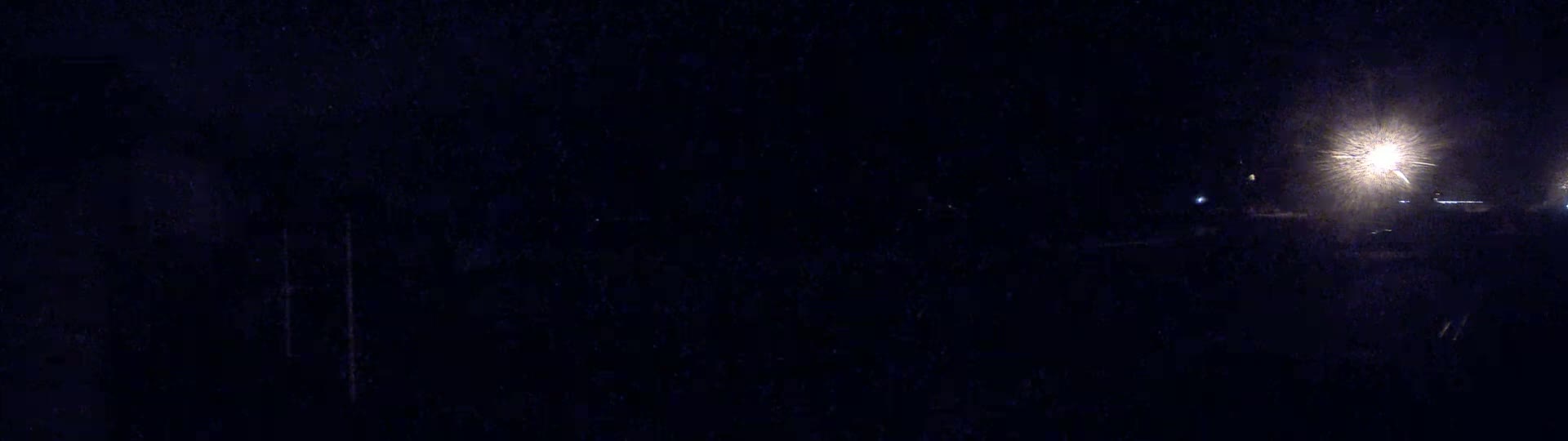 A nighttime outdoor scene shows a bright light source in the distance, illuminating a dark and otherwise indistinct landscape.