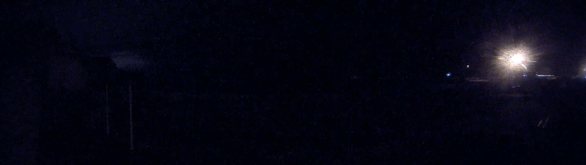 A dark, nighttime scene shows a bright light source in the distance, with a very dark foreground.