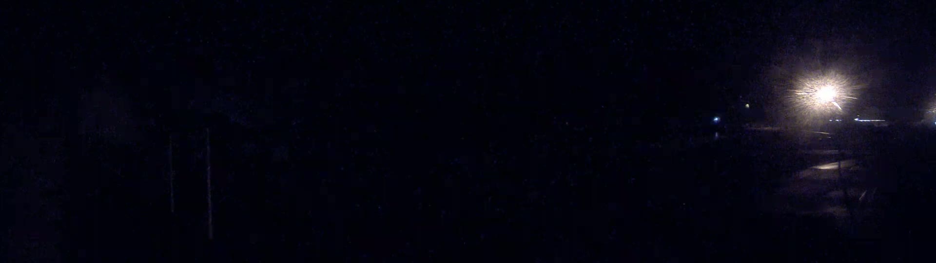 A dark, nighttime scene shows bright lights in the distance, possibly from streetlights, with a suggestion of snow or precipitation obscuring visibility.