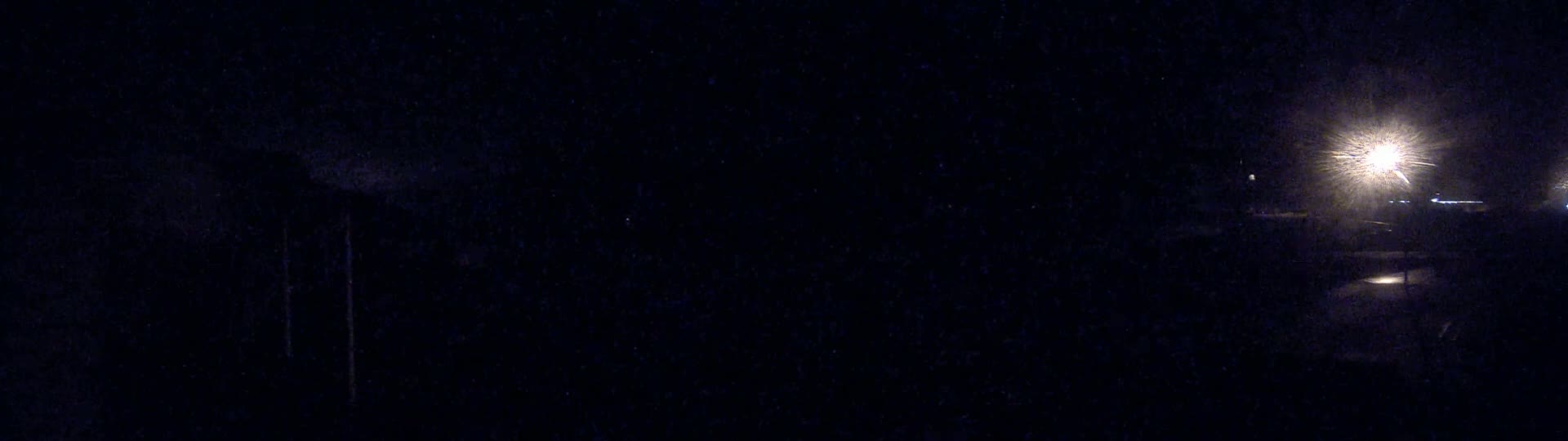 A dark, nighttime scene shows a bright light in the distance illuminating a seemingly empty area.